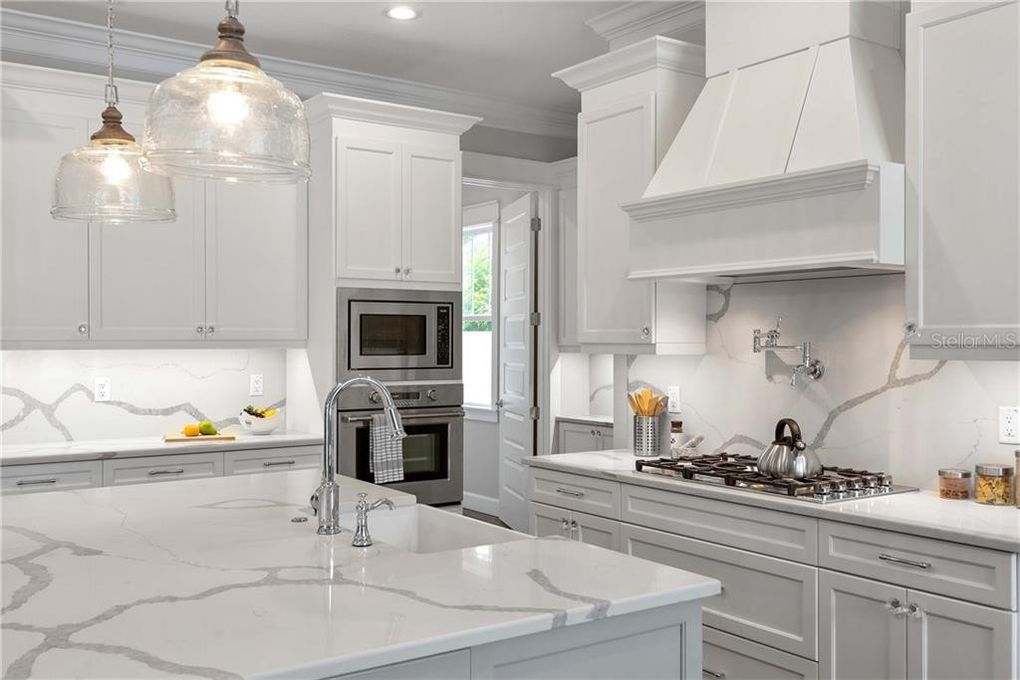 Bright white modern kitchen with marble island, gray cabinets, pendant lights, and stainless appliances