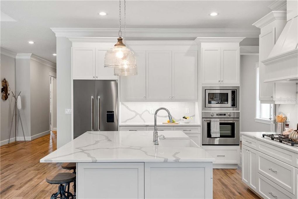 Bright modern white kitchen with marble island, stainless steel appliances, and hardwood floors