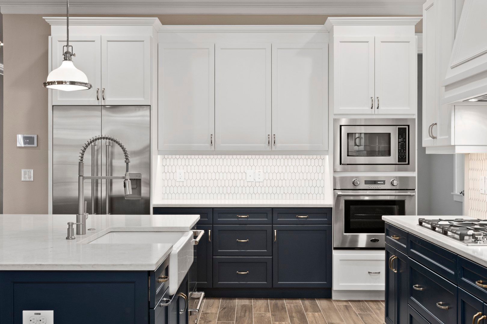 Modern kitchen with navy and white cabinets, marble countertops, and stainless steel appliances.