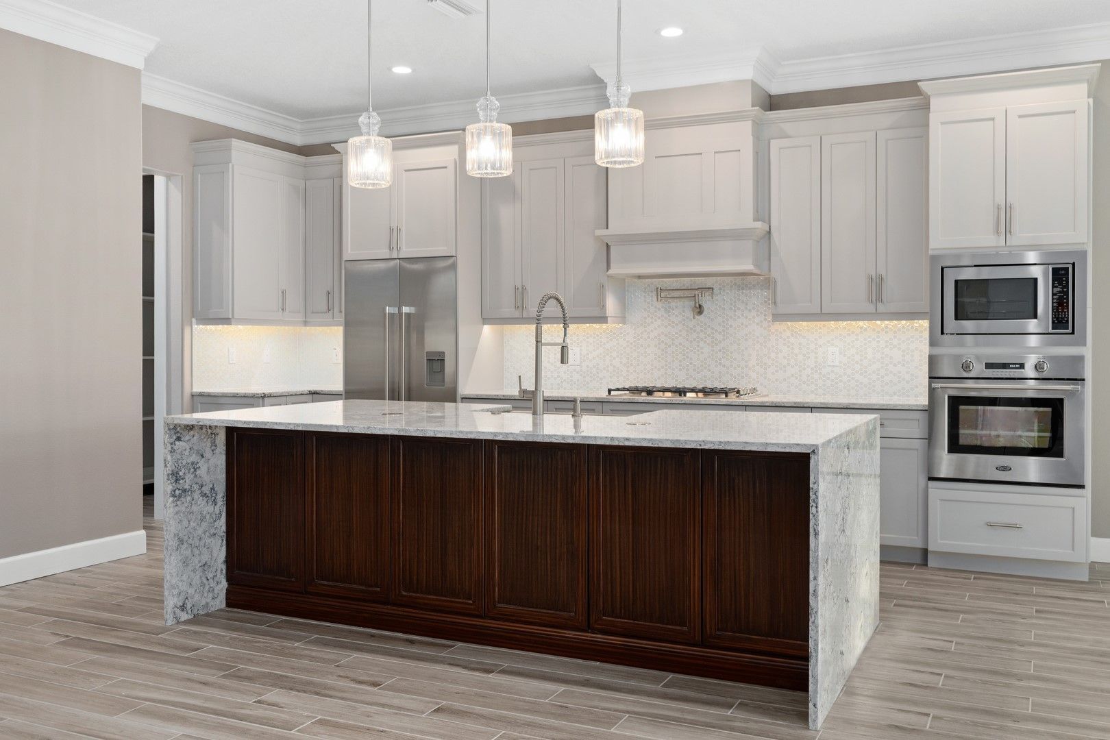 Modern kitchen with white cabinets, marble island, pendant lights, and stainless steel appliances