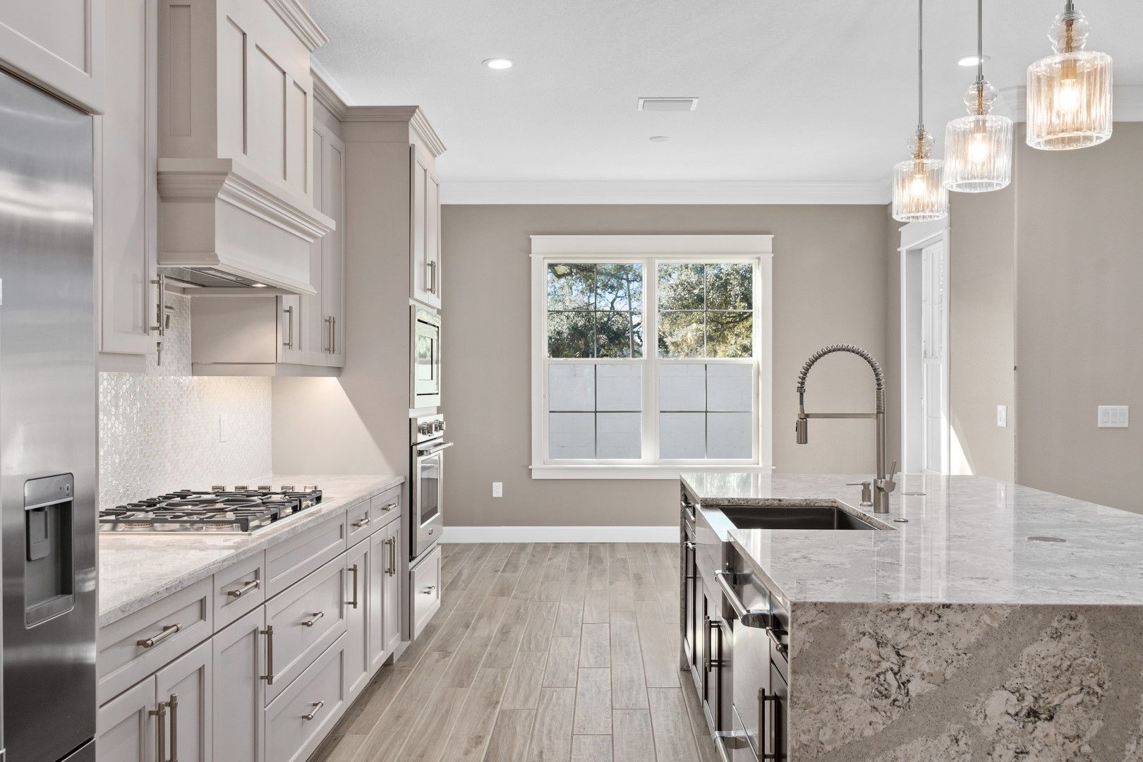 Bright modern kitchen with white cabinets, marble island, pendant lights, and a window at the end.