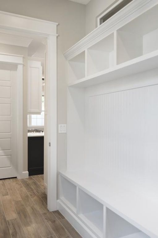 Bright white built-in mudroom bench with cubbies and beadboard paneling in a hallway, with wood-look flooring.