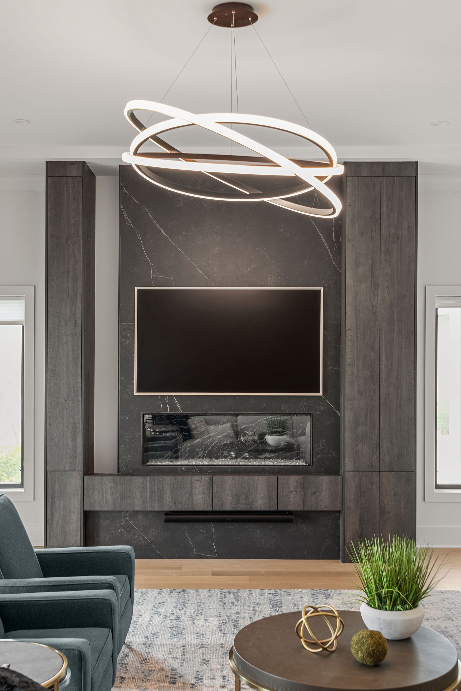 Modern living room with a wall-mounted TV, dark wood fireplace, and sculptural ceiling light