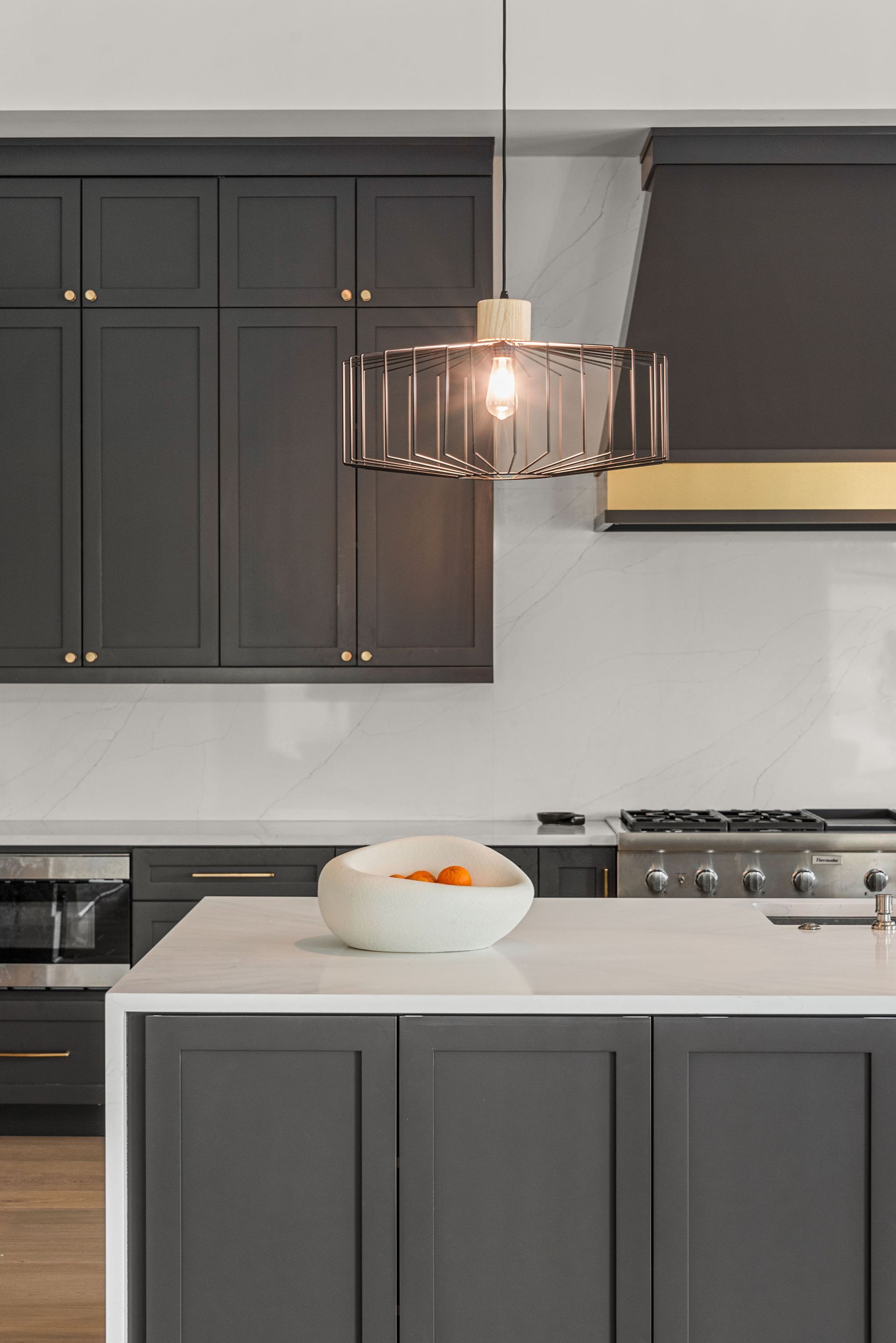 Modern kitchen with dark cabinets, white island, pendant light, and bowl of fruit on the counter.