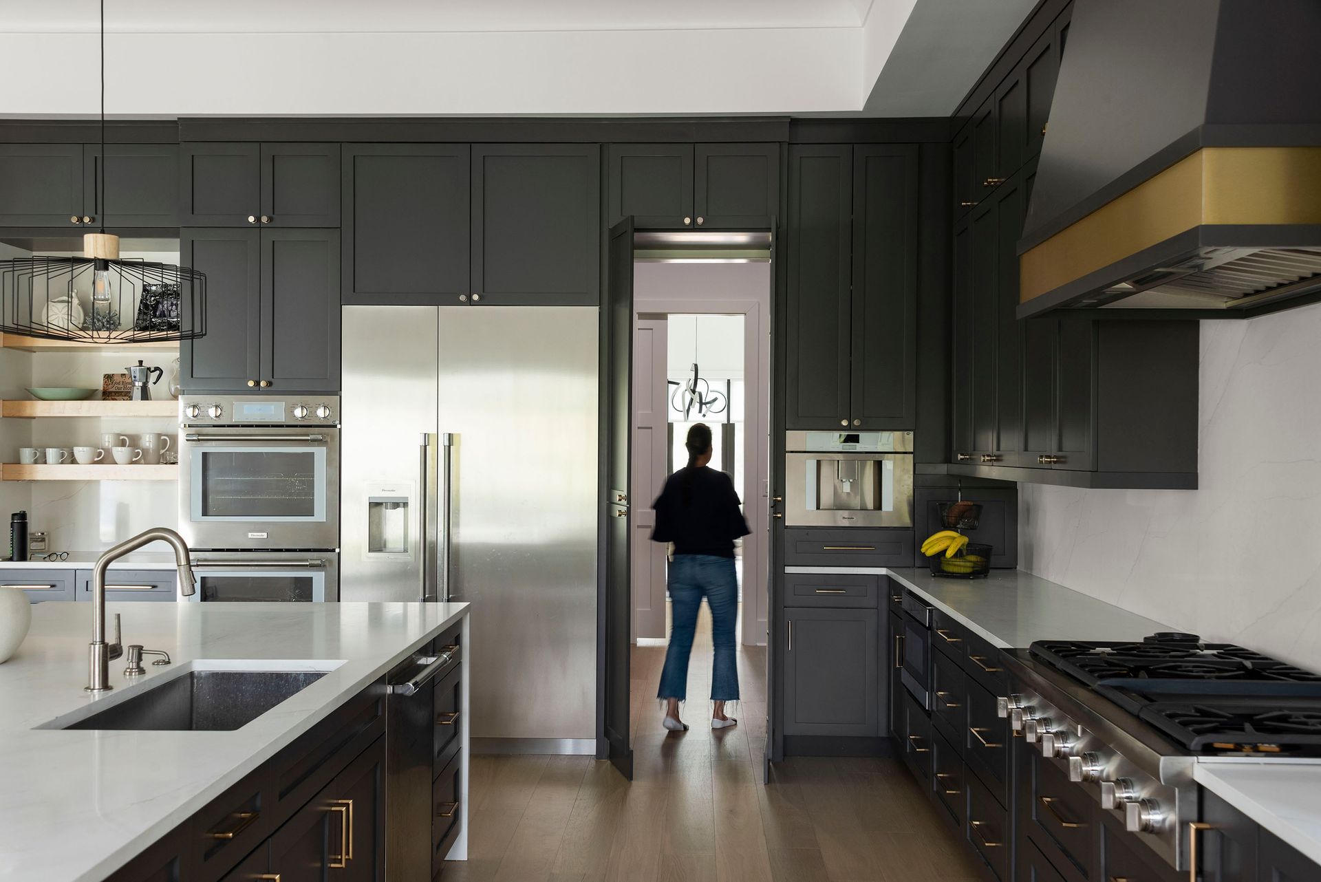 Modern kitchen with dark cabinets, stainless appliances, and a person standing at the refrigerator