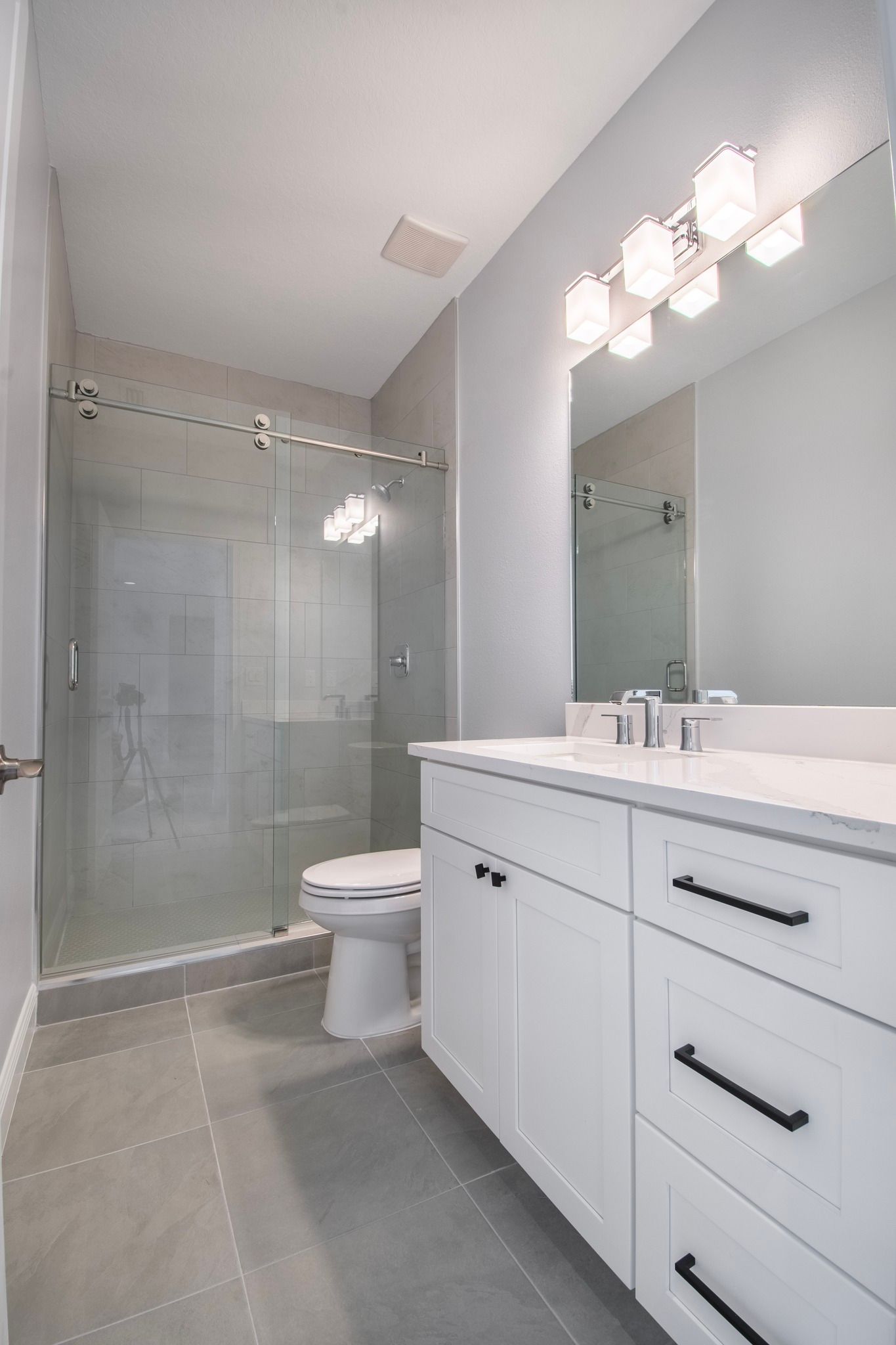Modern bathroom with glass shower, white vanity, and large mirror lights