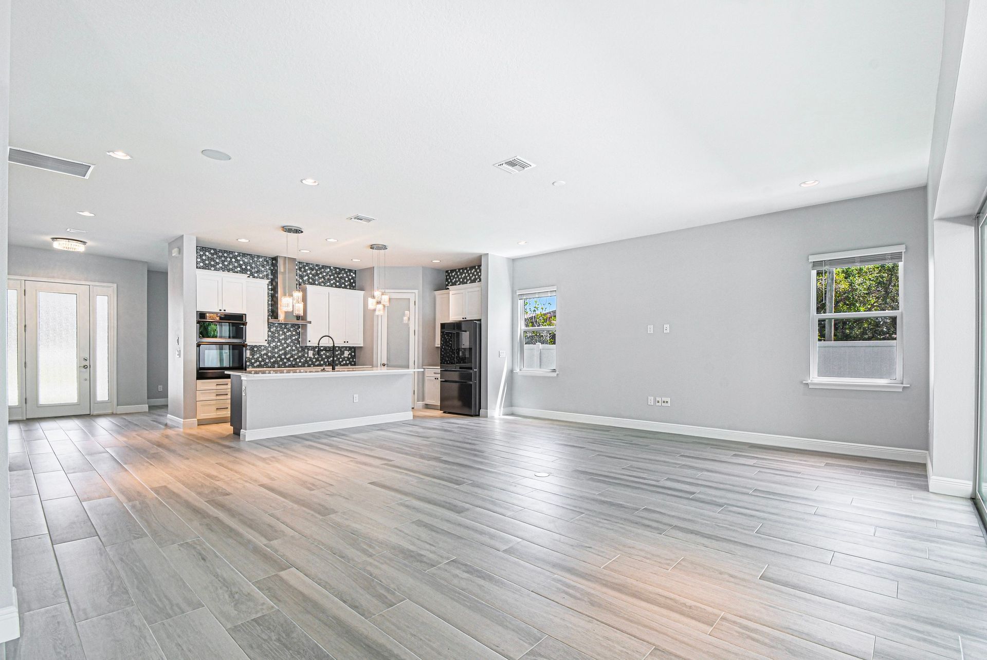 Bright open-plan living room with light wood floors, white kitchen, and gray walls.