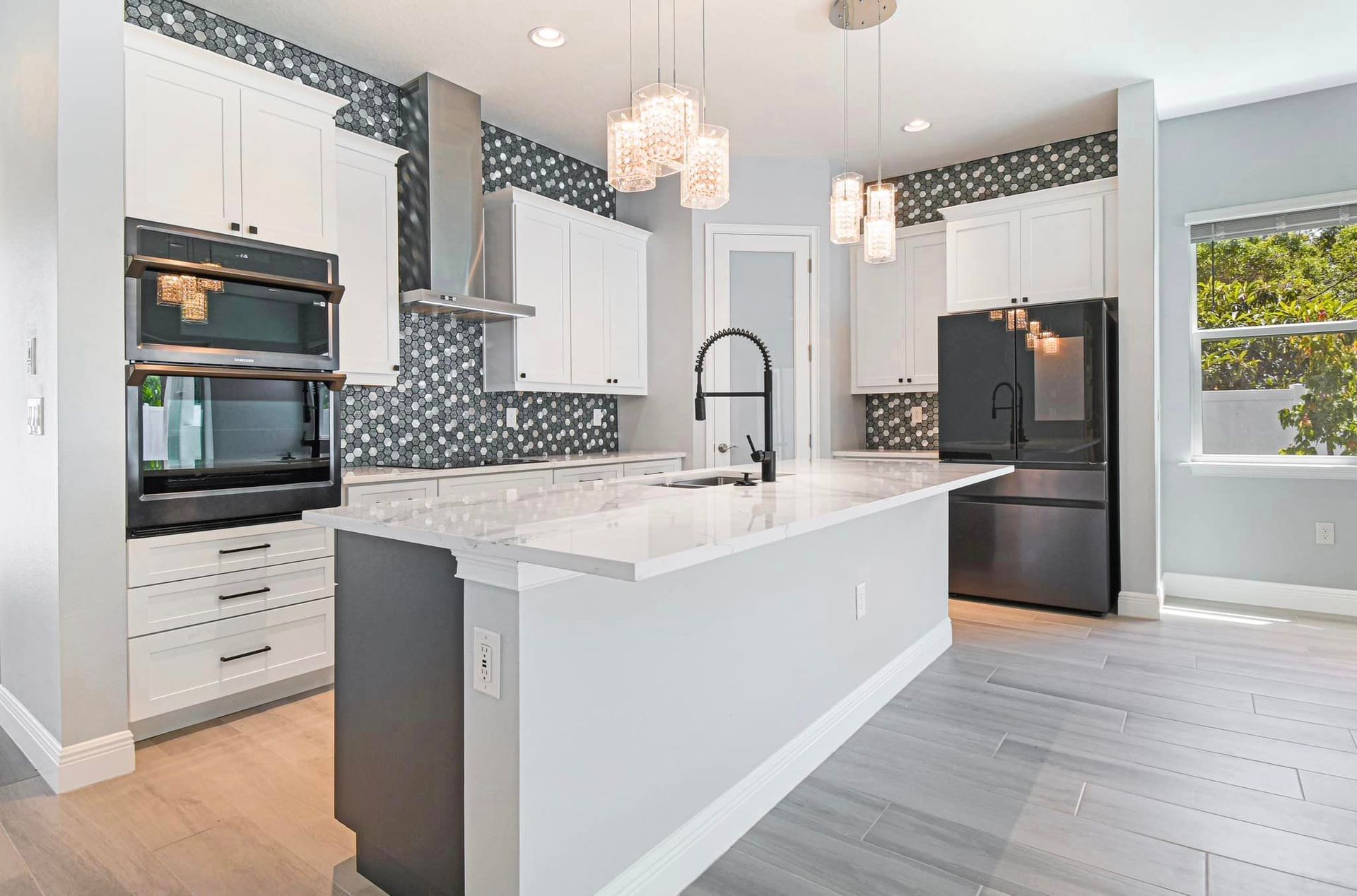 Bright modern kitchen with white cabinets, marble island, black appliances, and patterned backsplash
