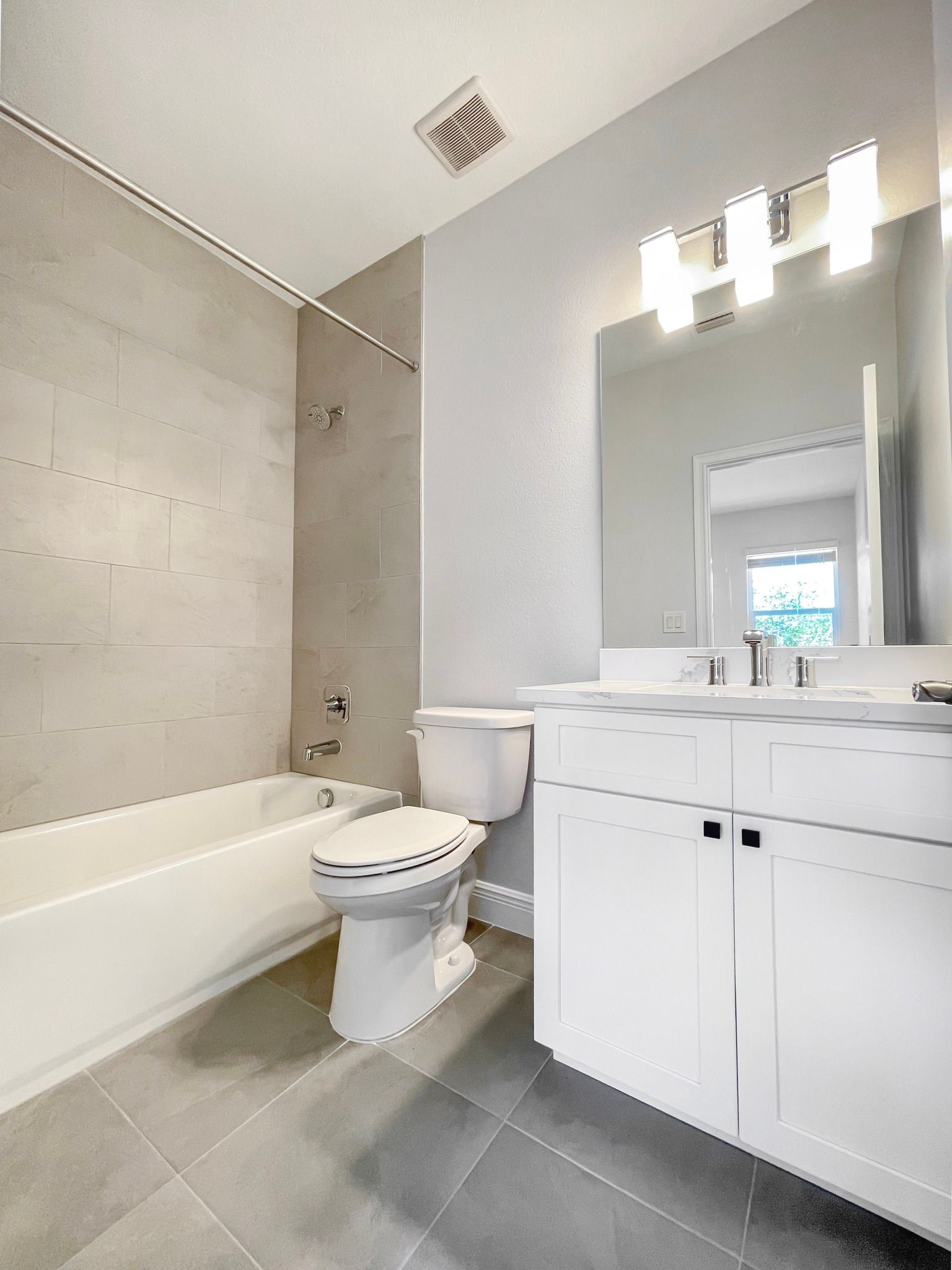 Bright bathroom with bathtub, toilet, and white vanity with lit mirror.