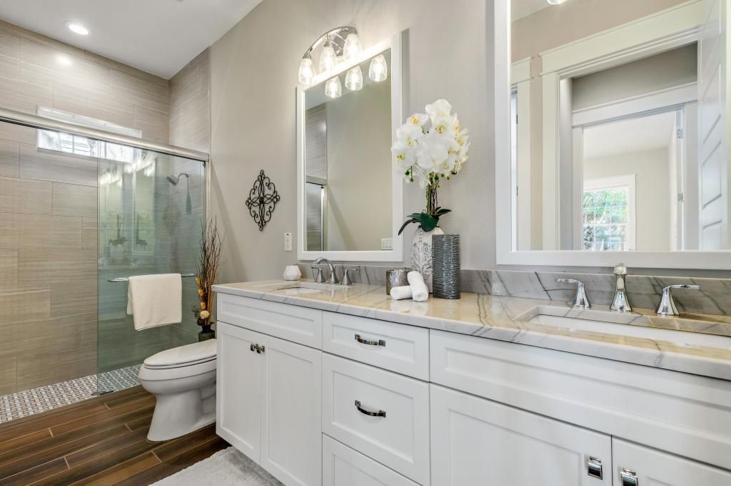 Bright bathroom with glass shower, white vanity, and large mirror with flowers.