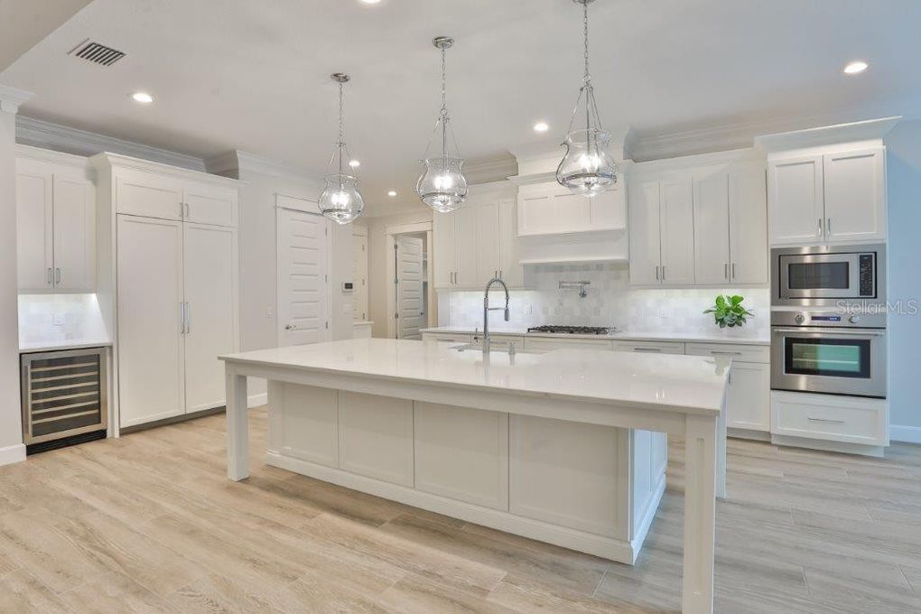 Bright white modern kitchen with large island, pendant lights, built-in appliances, and light wood floors