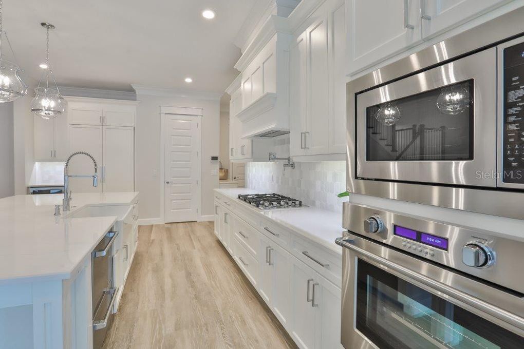 Bright modern white kitchen with stainless steel appliances, island, and light wood flooring