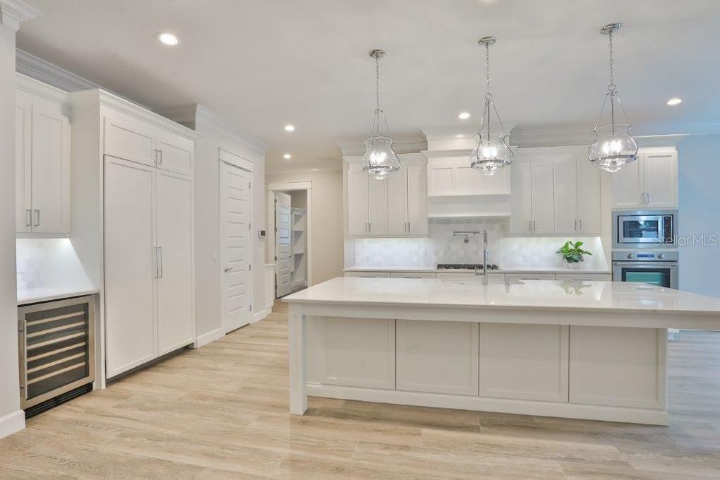 Bright white modern kitchen with island, pendant lights, and light wood flooring
