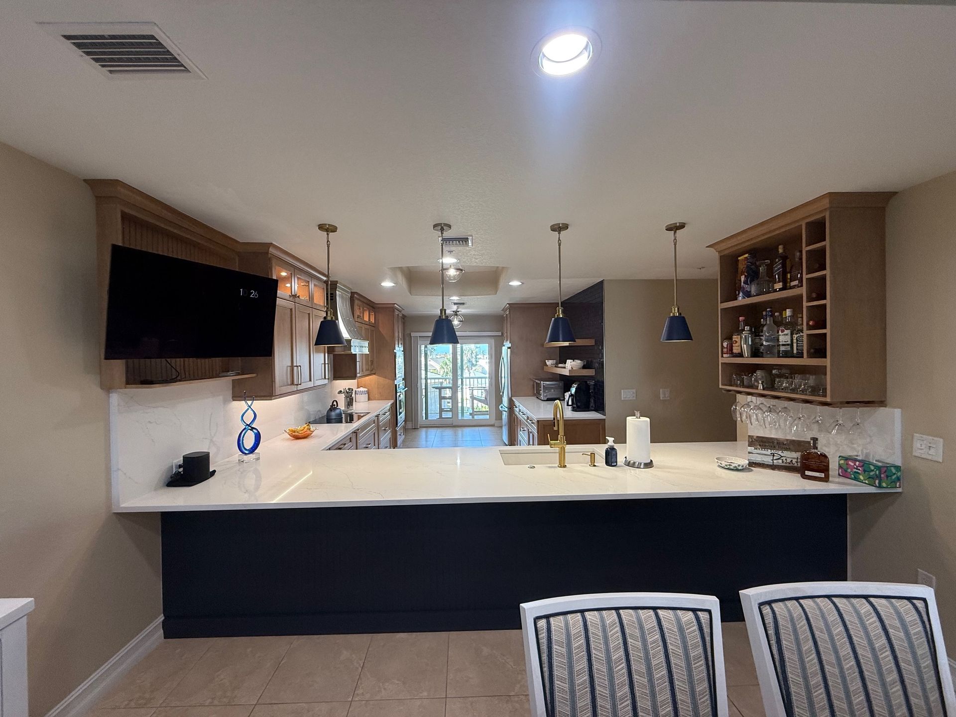 Modern kitchen with white island, dark cabinets, pendant lights, and wall-mounted TV.