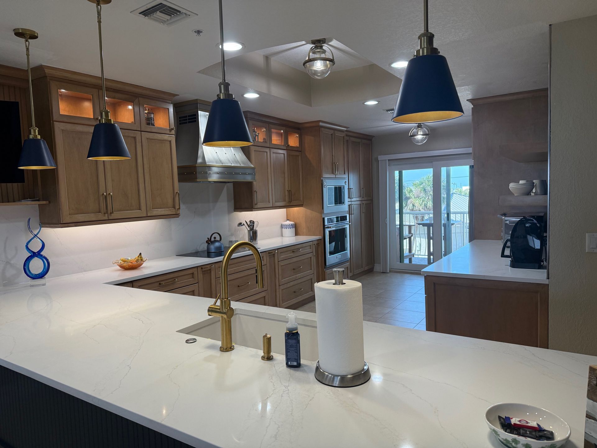 Modern kitchen with white island, wood cabinets, blue pendant lights, and sliding glass doors to a patio.
