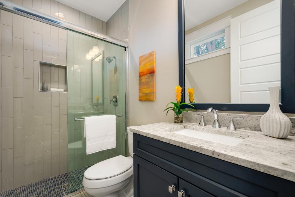 Modern bathroom with glass shower, toilet, and dark vanity with marble countertop