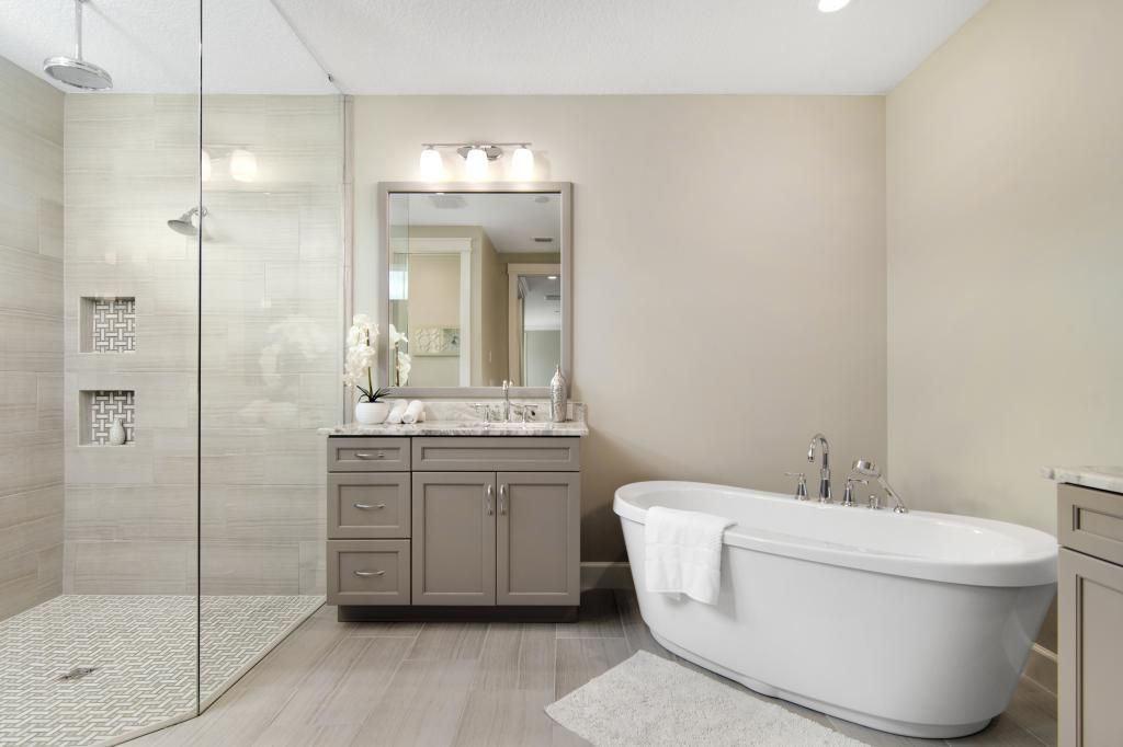 Modern beige bathroom with glass shower, vanity, mirror, and freestanding tub