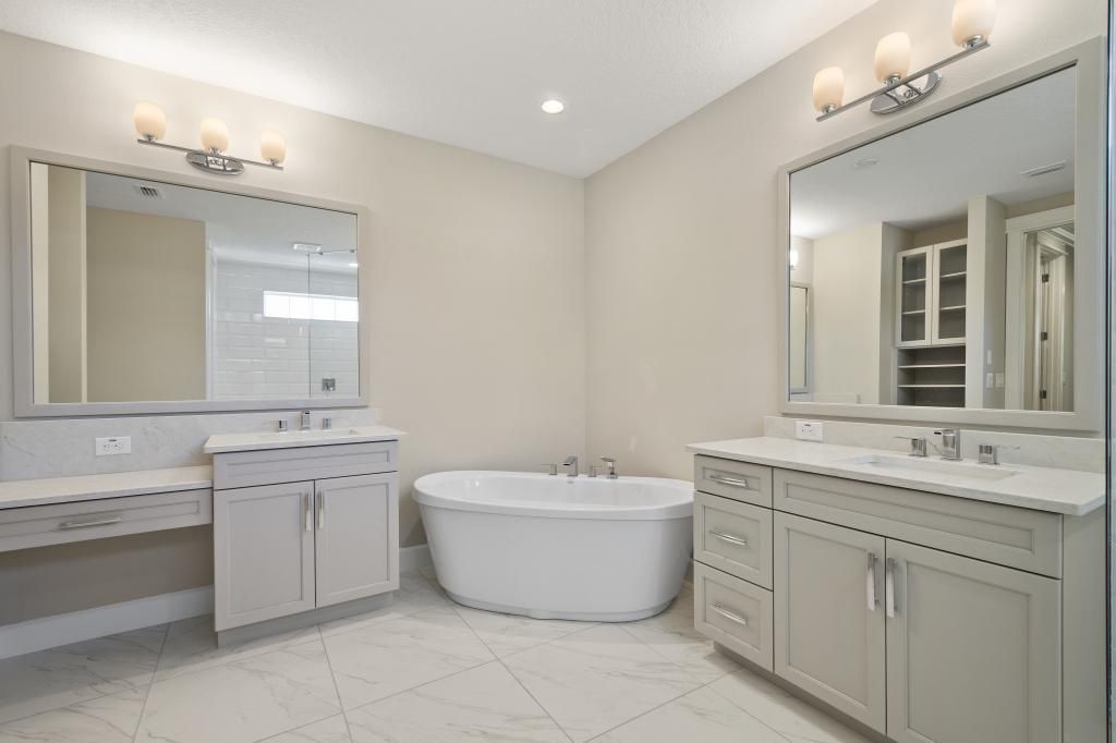 Bright white bathroom with double vanity, large mirrors, and a freestanding soaking tub