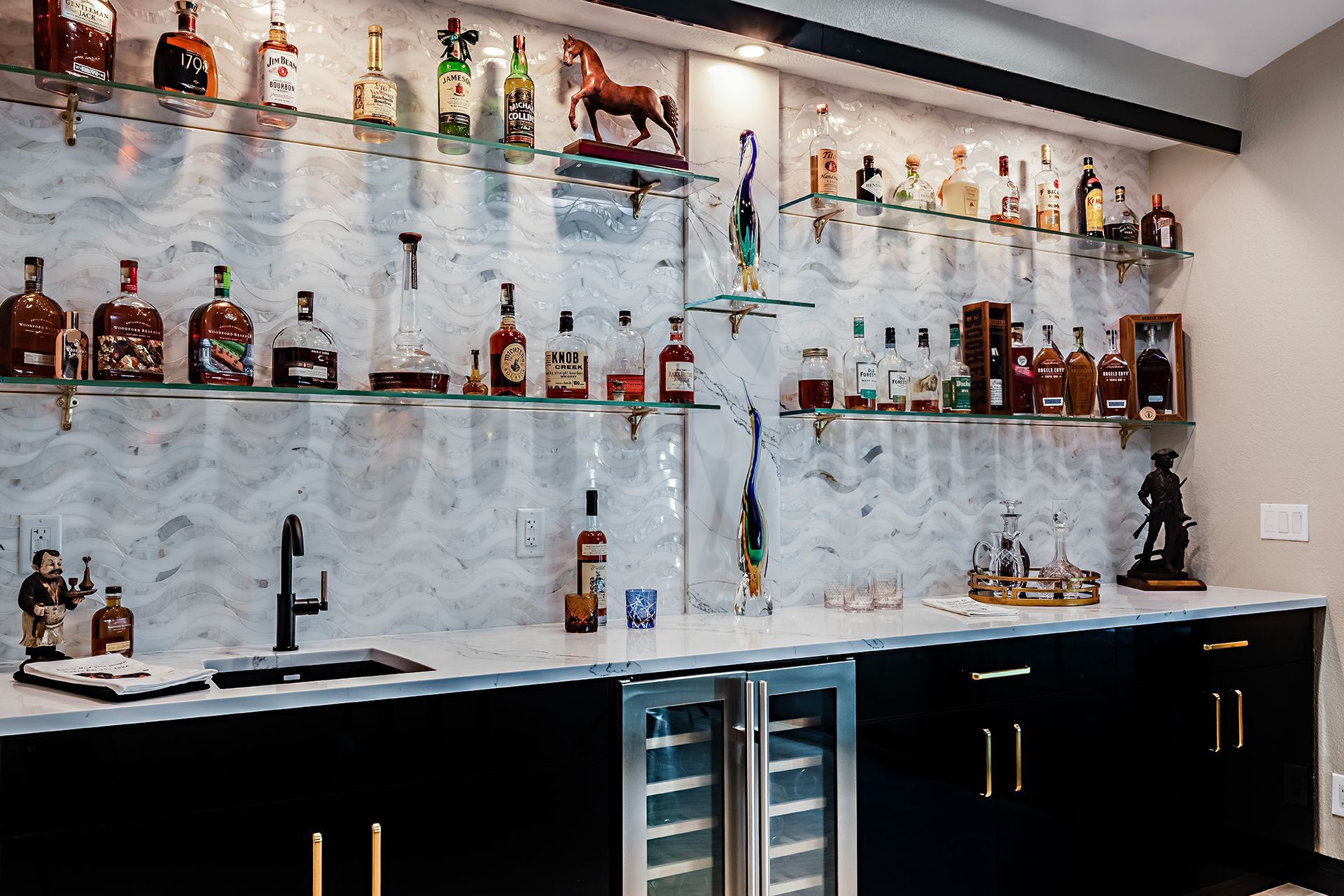 Bar with marble backsplash, shelves of liquor bottles, sink, and black cabinets