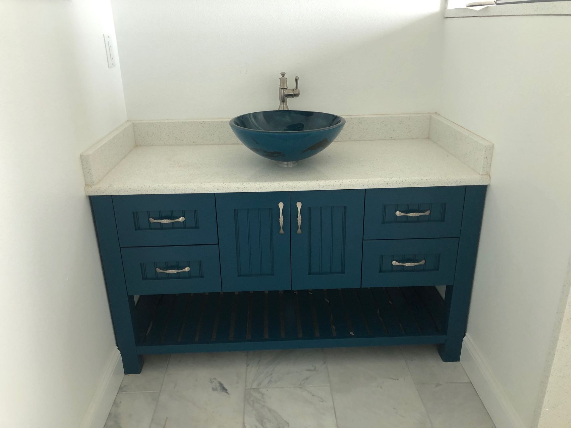 Blue bathroom vanity with white countertop and round sink in a small alcove