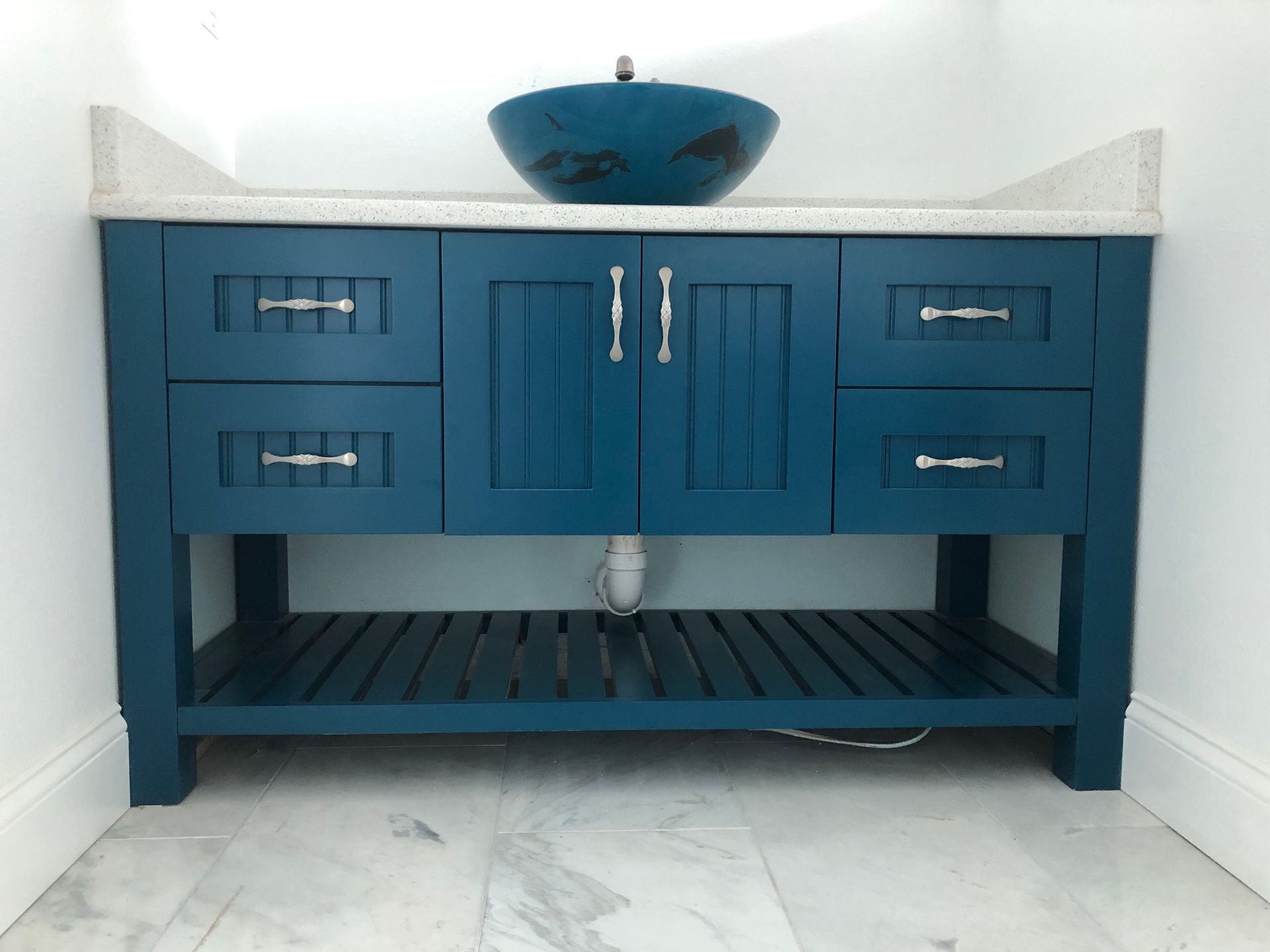 Blue bathroom vanity with black slatted shelf and white countertop in a corner.