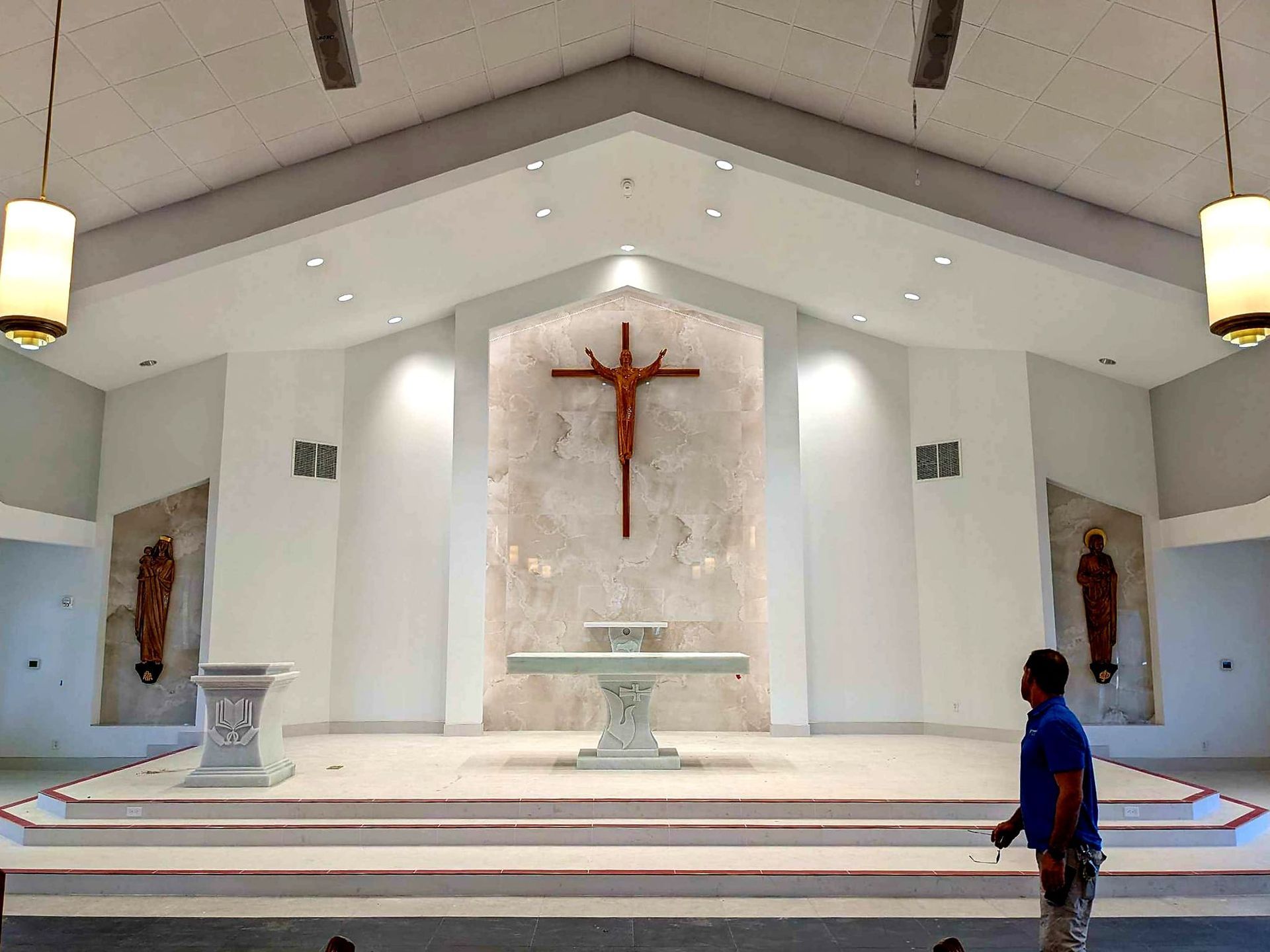 White church sanctuary with crucifix above altar, bright interior, and a person standing at right.