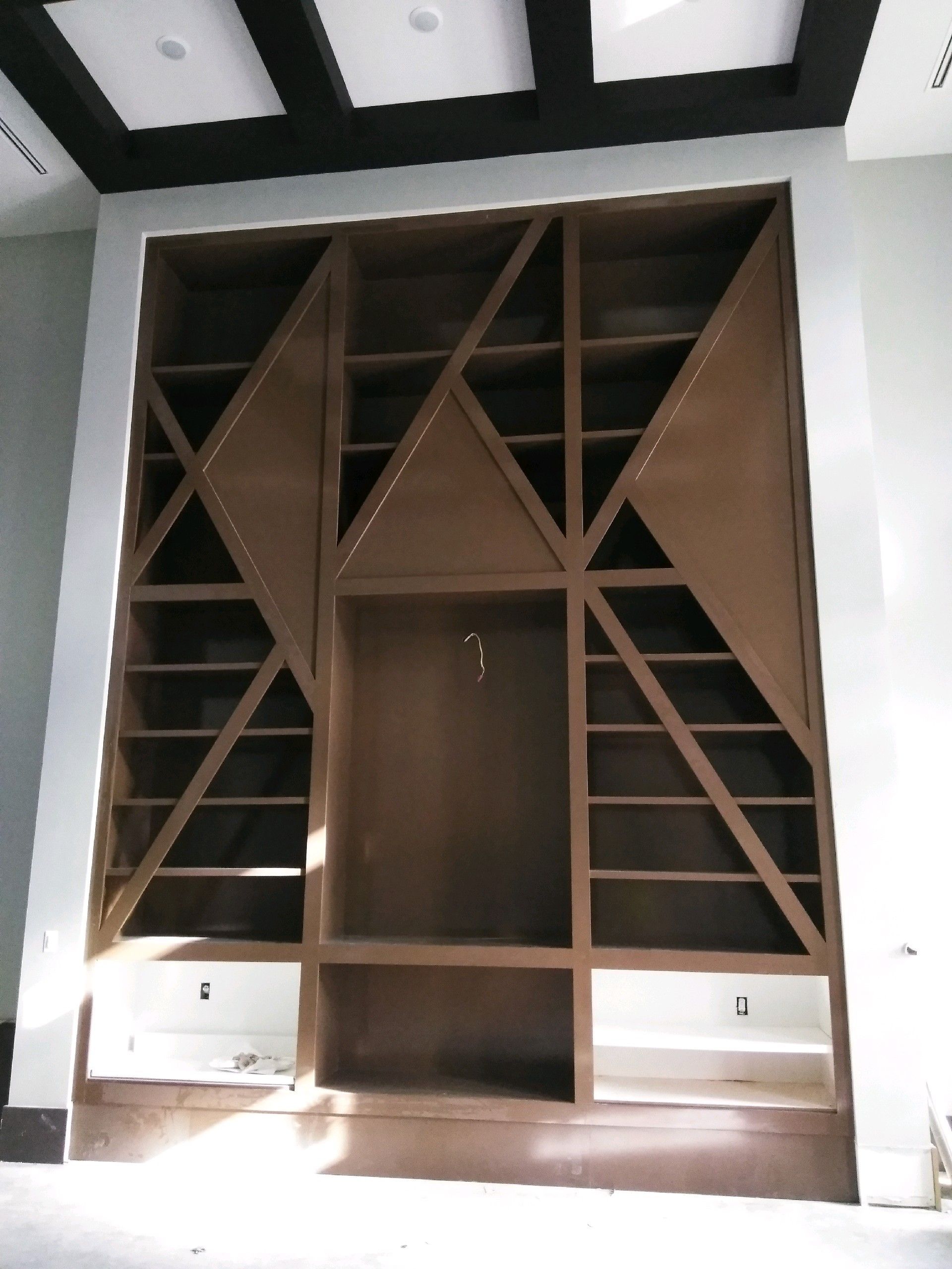 Brown geometric built-in shelving unit with open compartments and two white drawers at the bottom.