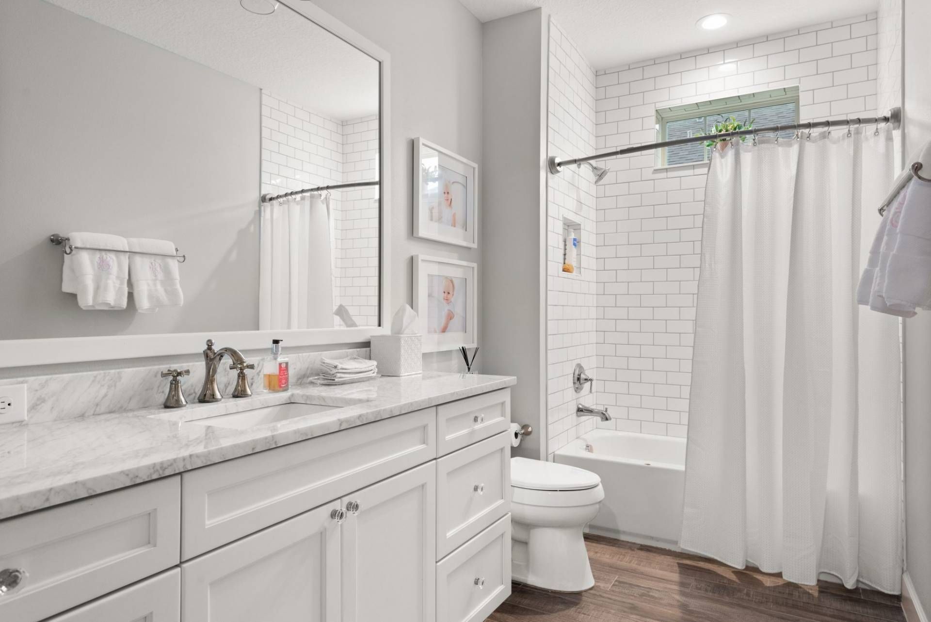 Bright white bathroom with double vanity, large mirror, and shower curtain beside a toilet