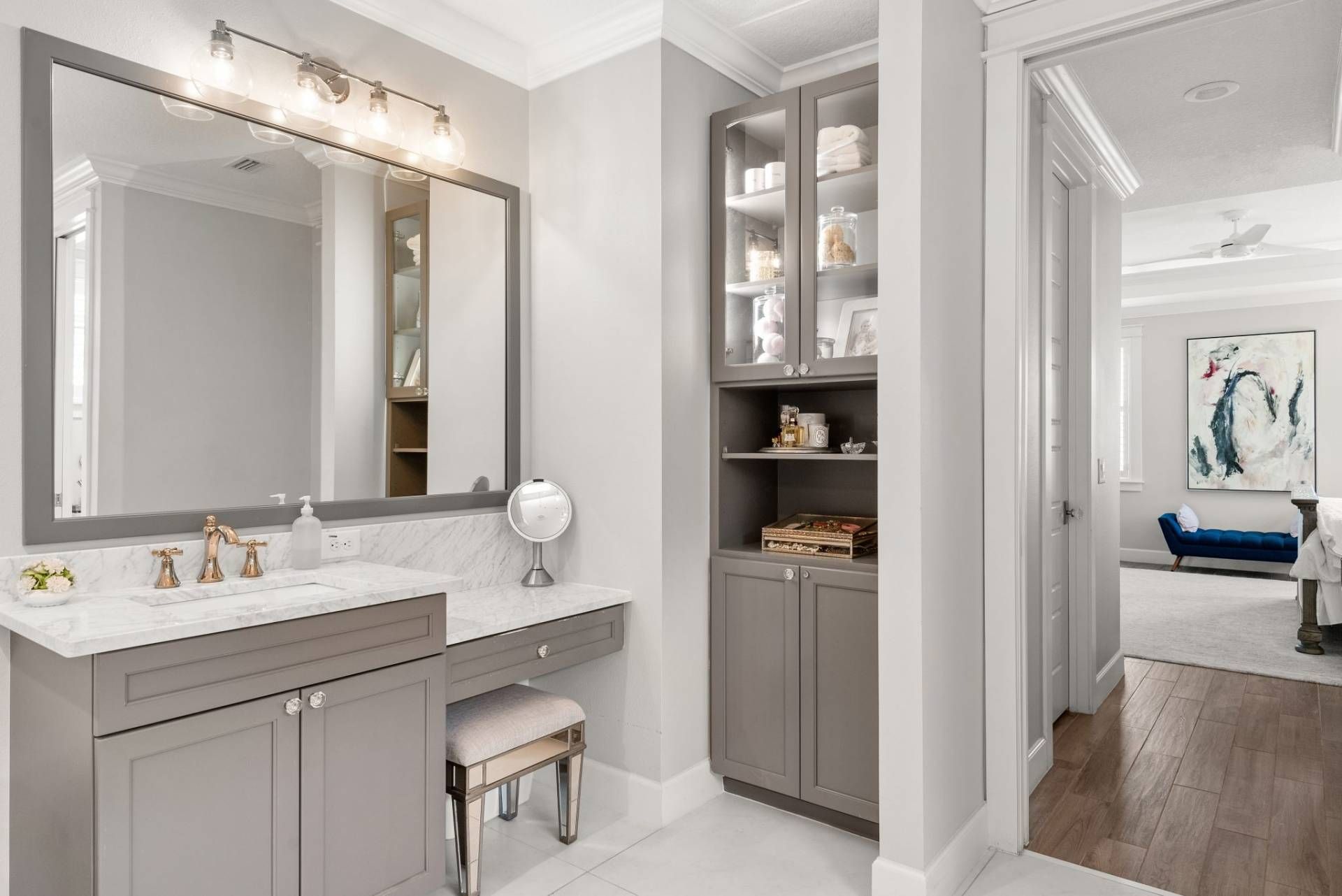 Elegant gray bathroom with double vanity, large mirror, storage cabinet, and doorway to a bedroom.