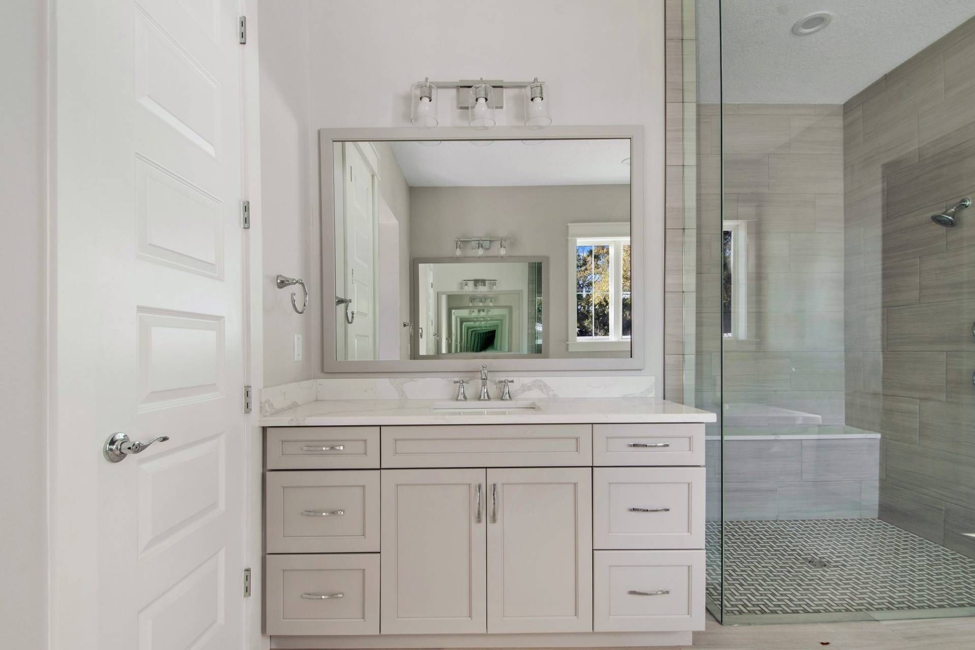 Modern bathroom vanity with large mirror, white cabinets, and glass shower enclosure