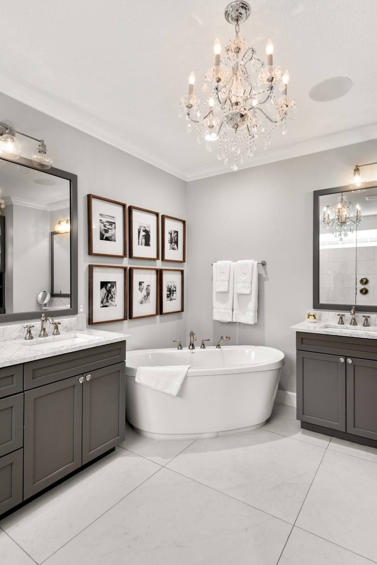Elegant gray bathroom with freestanding tub, double vanity, chandelier, and framed wall art