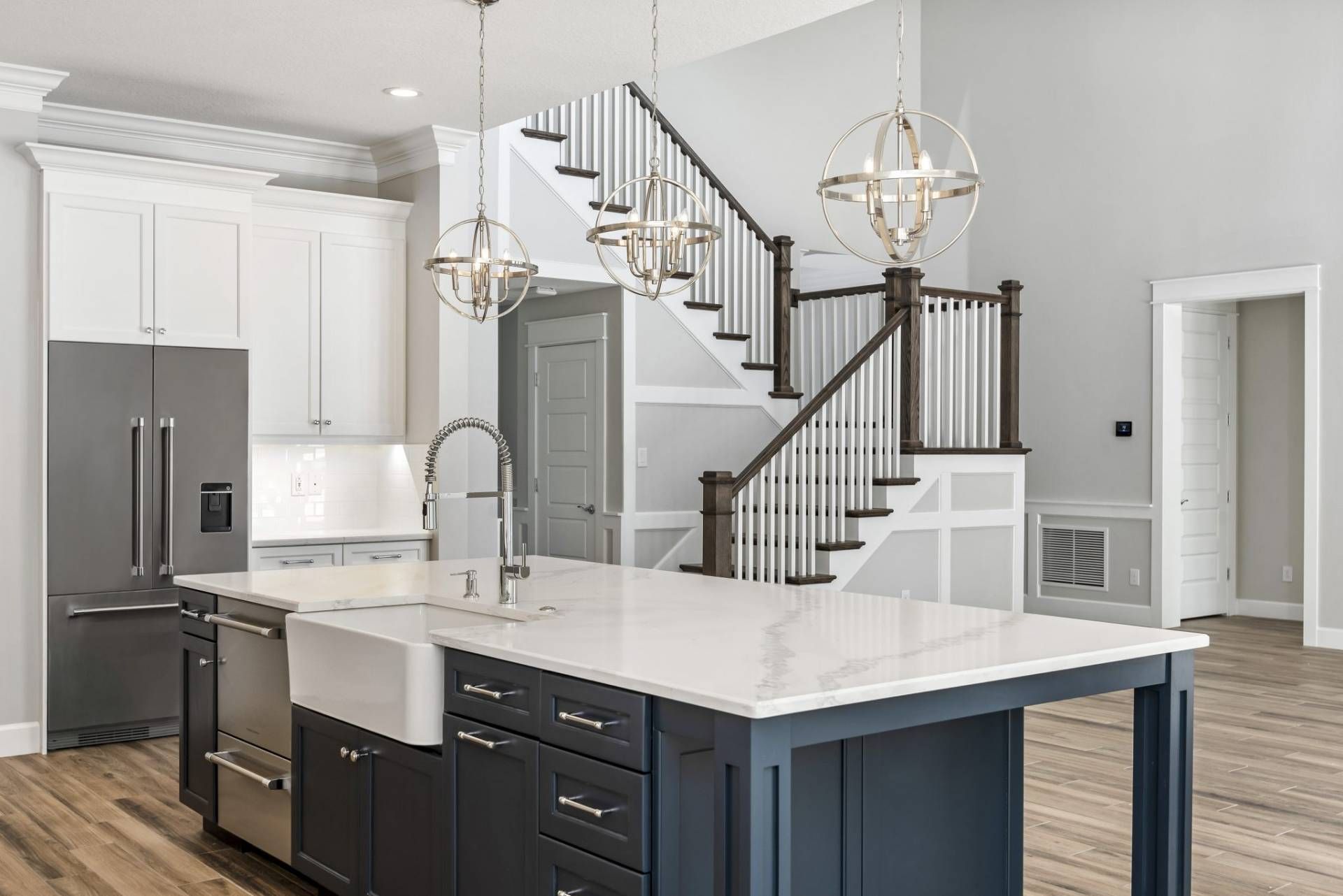 Modern kitchen with dark island, white cabinets, stainless appliances, and staircase in background