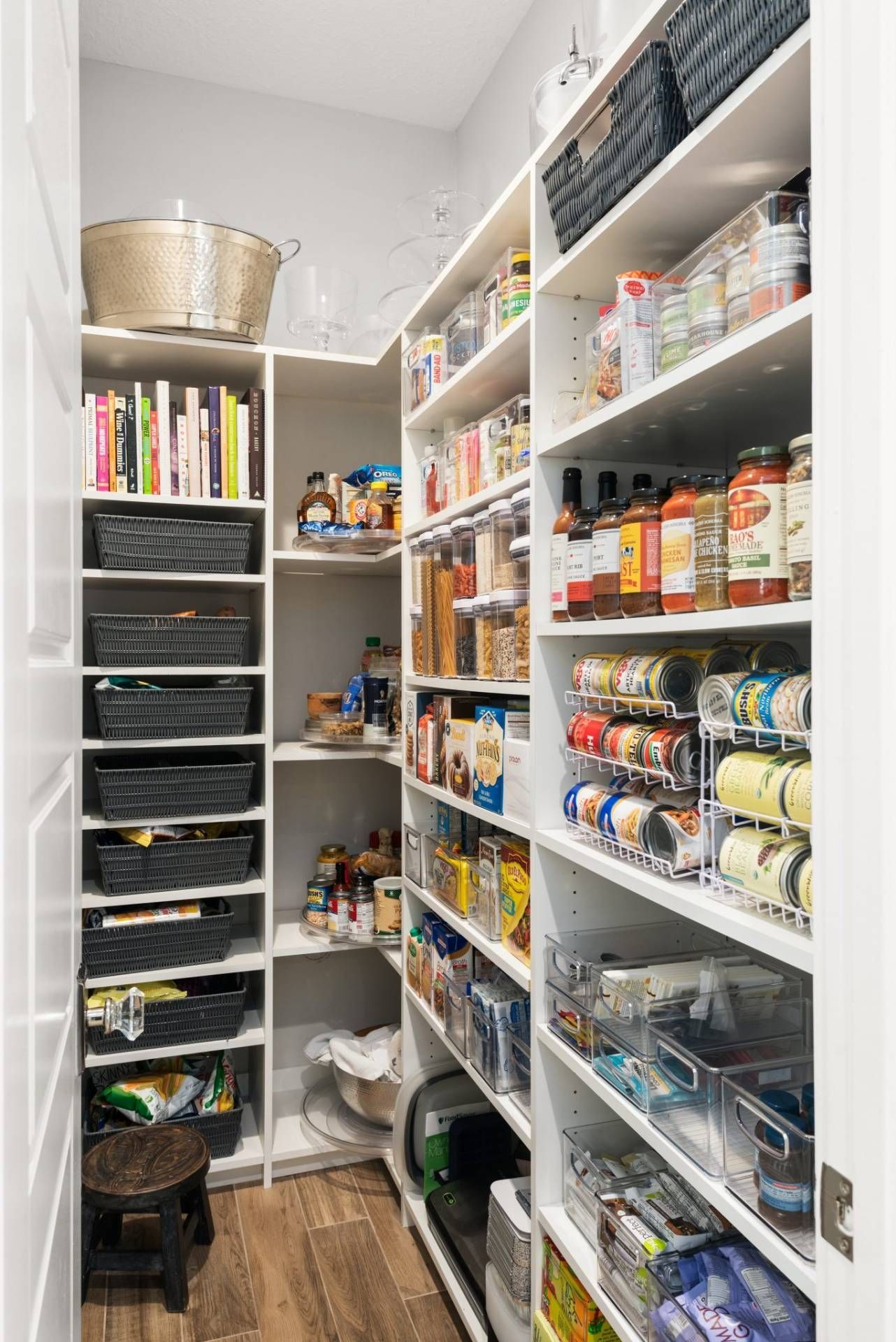 Narrow pantry with white shelves, baskets, canned goods, and stacked storage bins.