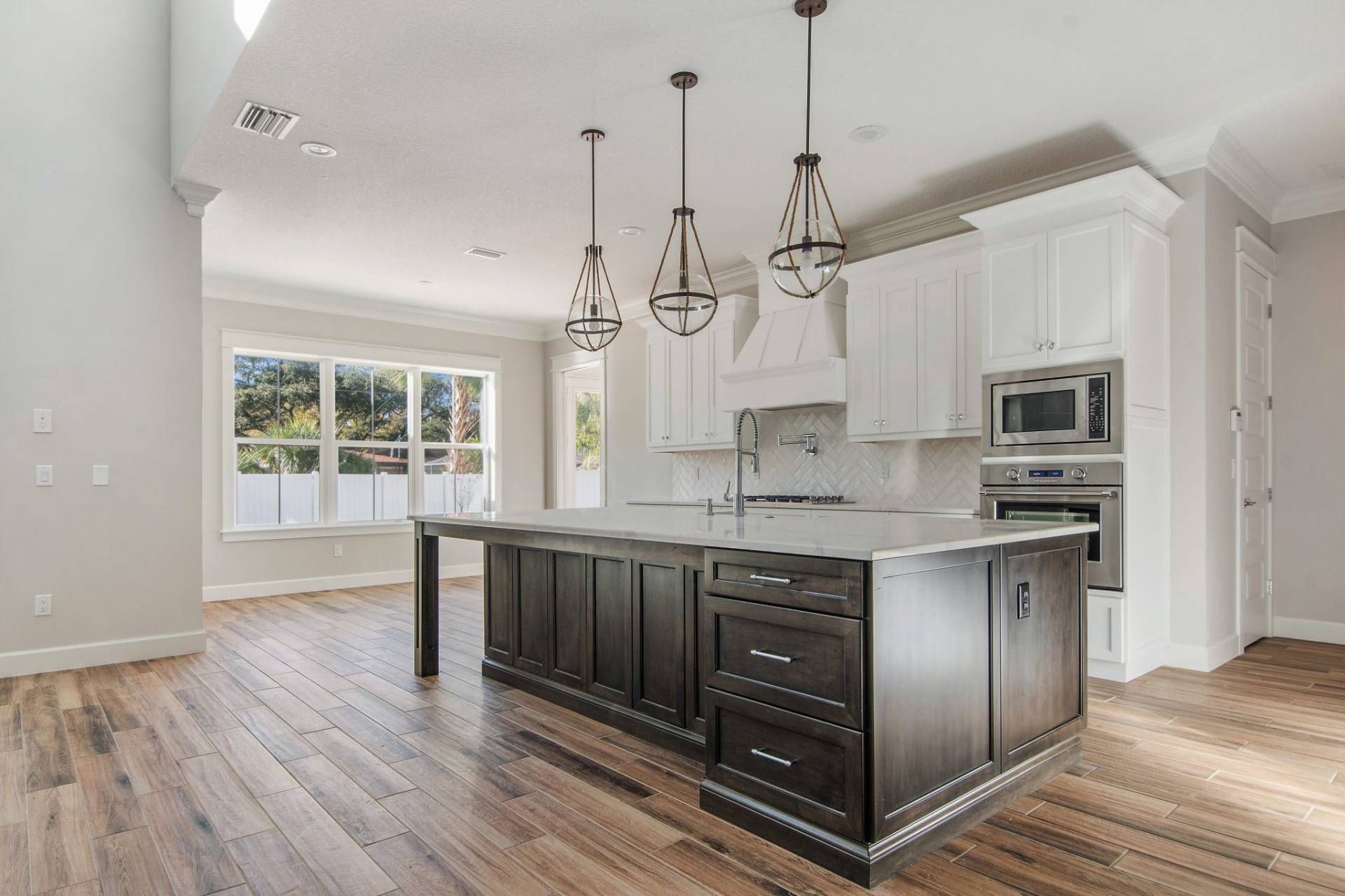 Modern kitchen with dark island, white cabinets, pendant lights, and hardwood floors