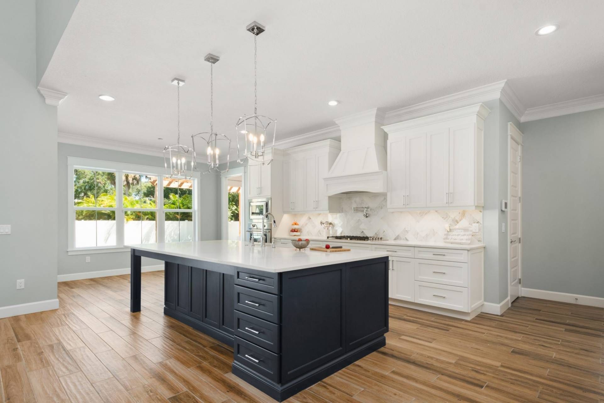 Bright modern kitchen with navy island, white cabinets, marble counters, and hardwood floors