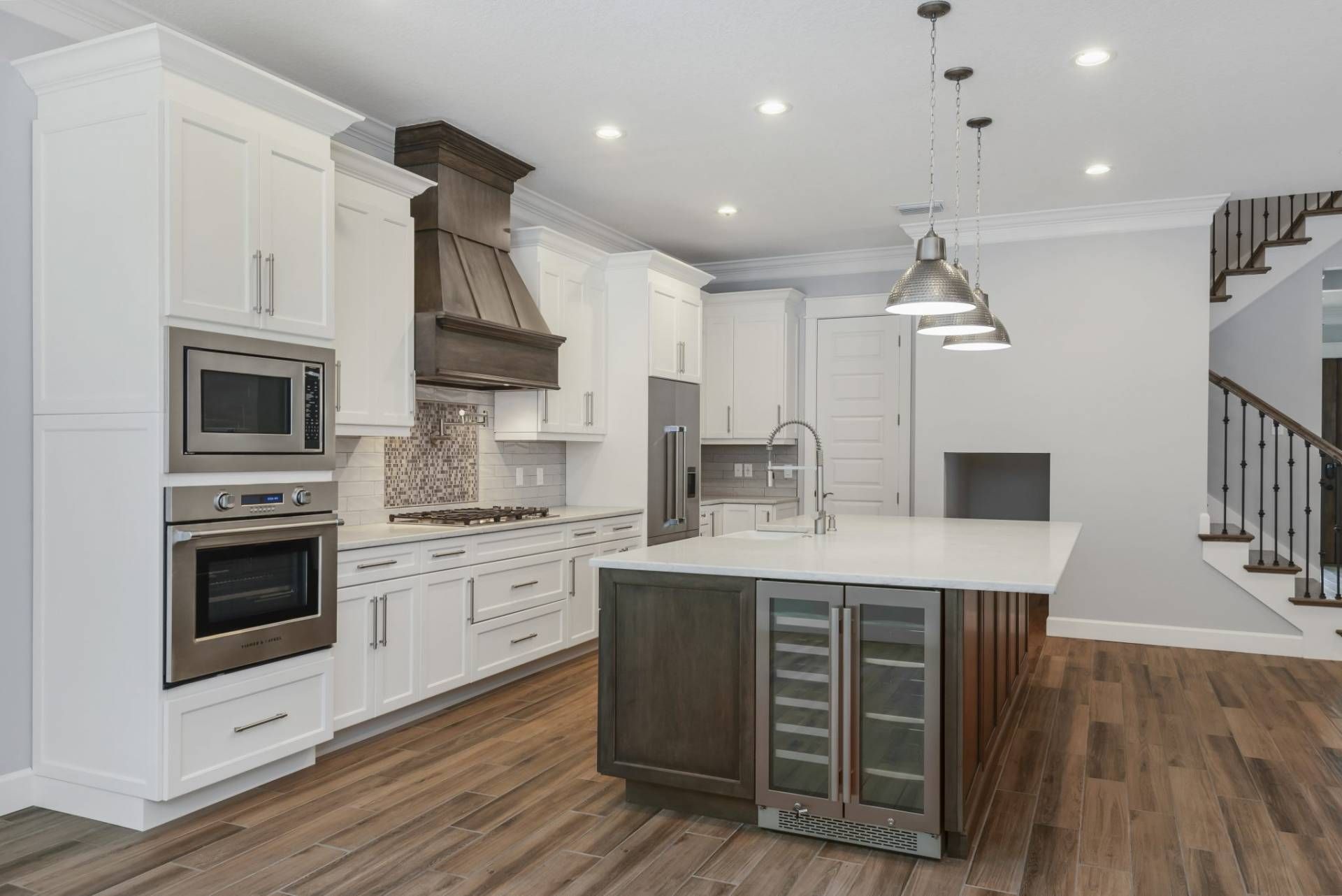 Modern white kitchen with island, stainless appliances, pendant lights, and hardwood floors