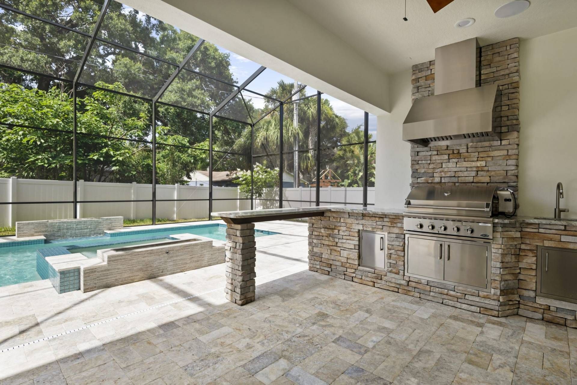 Covered patio with stone grill, poolside seating, and screened-in backyard view