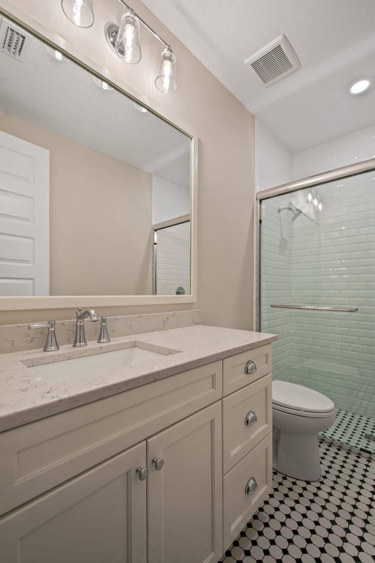 Bright bathroom with vanity, large mirror, toilet, and glass shower with green-tinted tile.