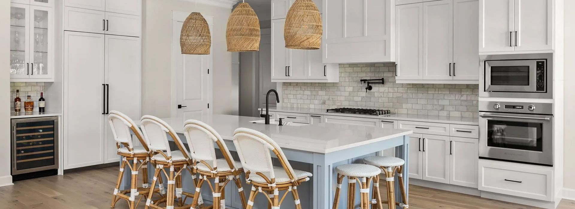 Modern white kitchen with island, bar stools, pendant lights, and built-in double ovens