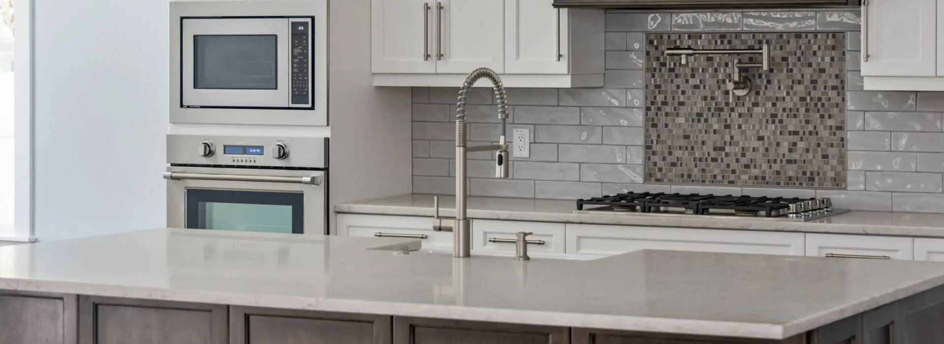 Modern white kitchen with island, stainless sink, built-in microwave, and mosaic tile backsplash
