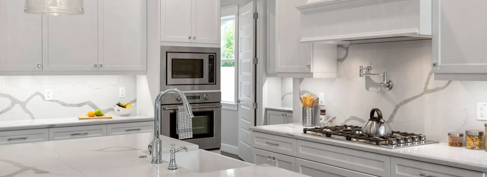 Bright white modern kitchen with marble counters, stainless appliances, and a vase on the island
