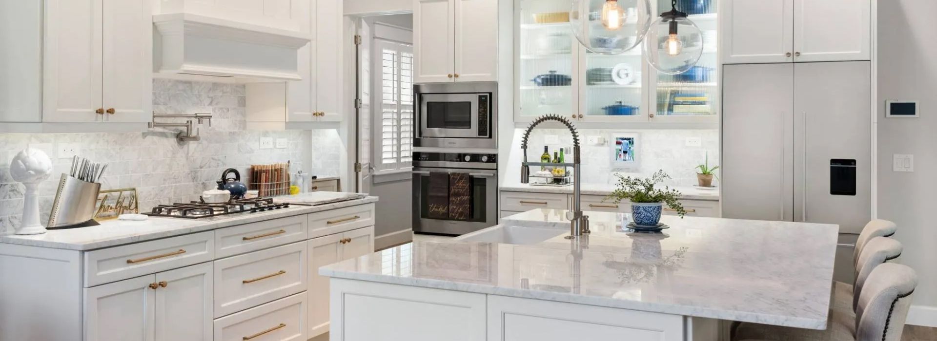 Bright white modern kitchen with island, stainless steel appliances, and glass-front cabinets
