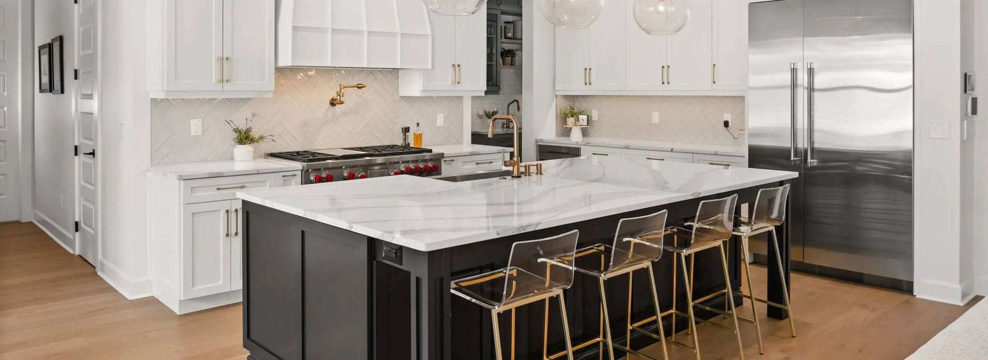 Modern white kitchen with marble island, black cabinets, gold stools, and stainless steel refrigerator
