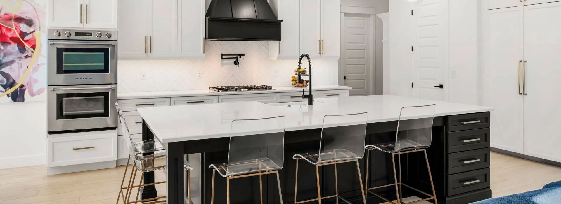 Modern white kitchen with island, black stools, stainless appliances, and pendant lights