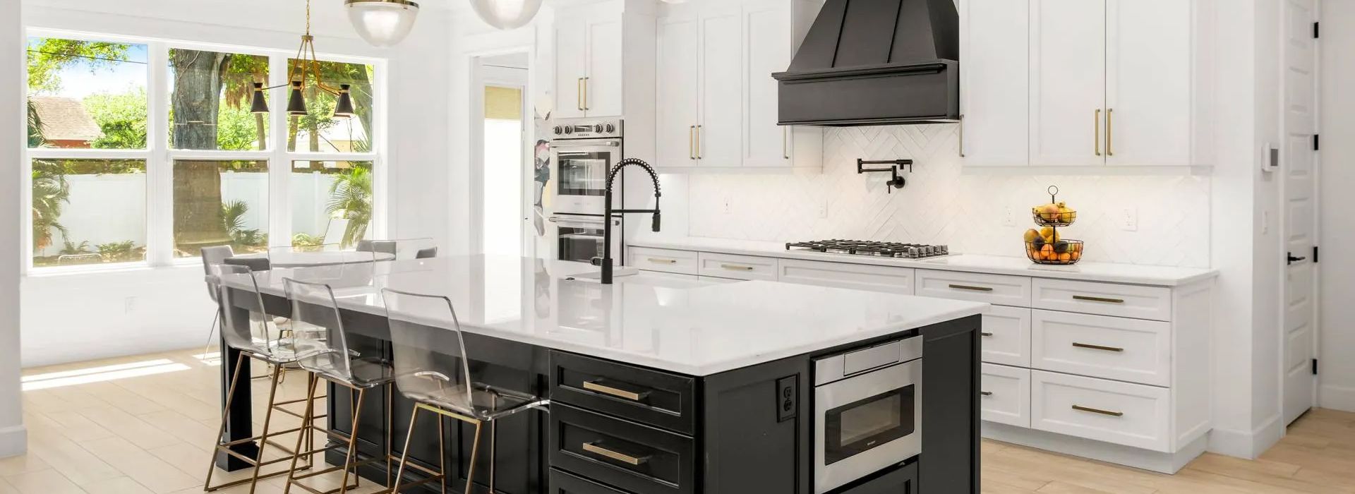 Bright modern kitchen with white cabinets, marble island, and black stools by a window