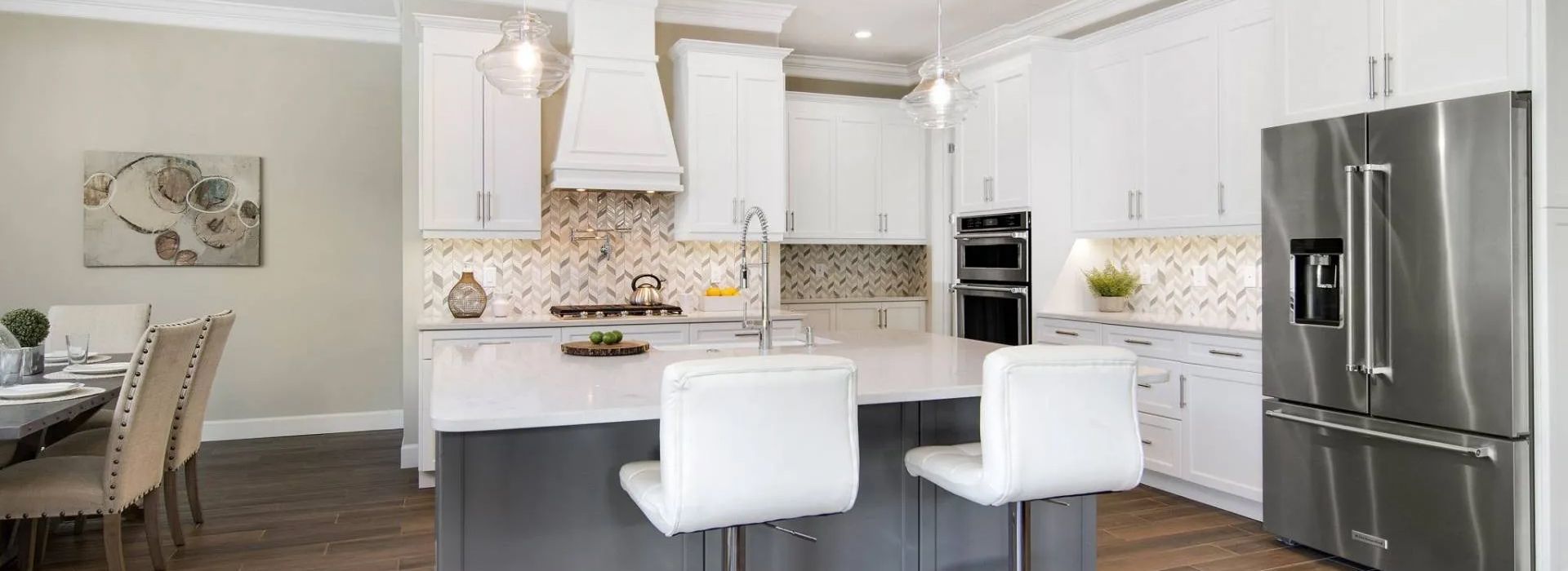 Modern white kitchen with island, pendant lights, bar stools, and stainless steel refrigerator