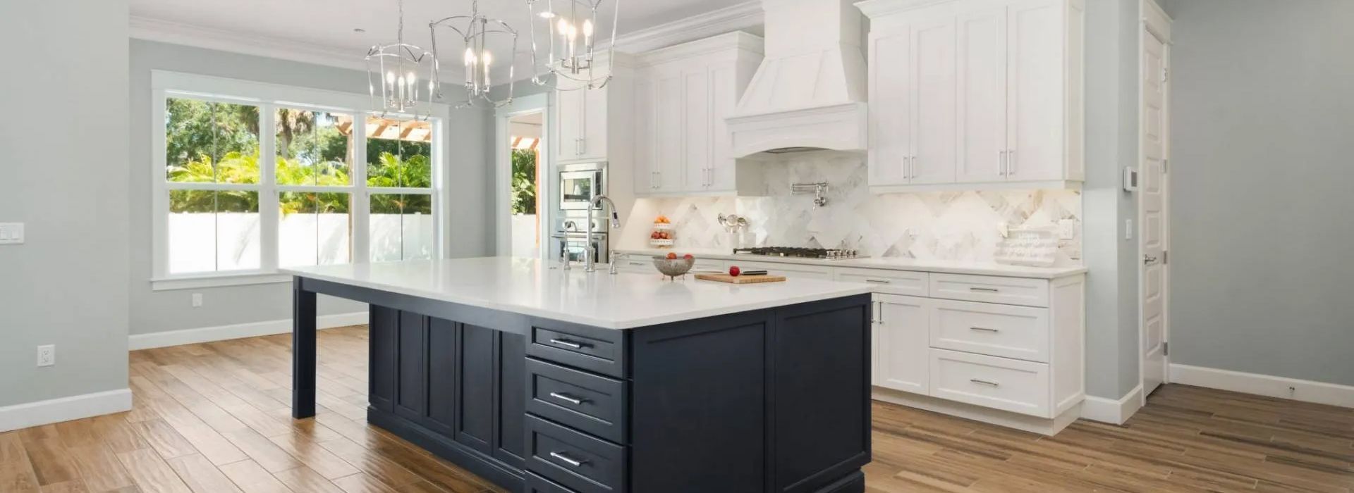 Bright white kitchen with dark island, marble counters, and wood floors in an open, sunlit space