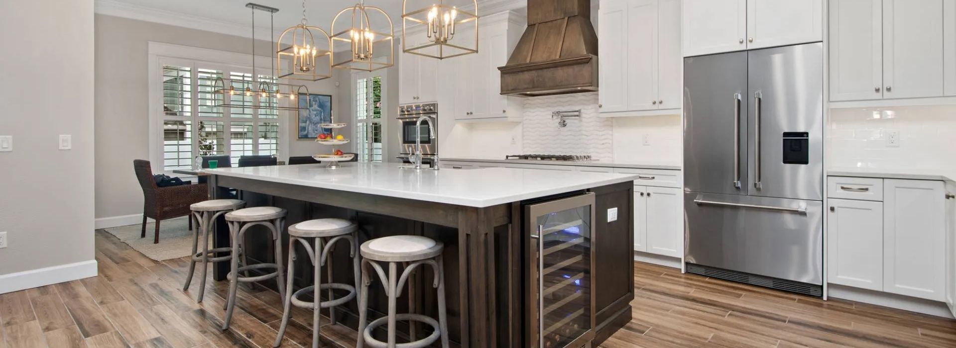 Bright modern kitchen with white cabinets, island seating, stainless steel fridge, and pendant lights