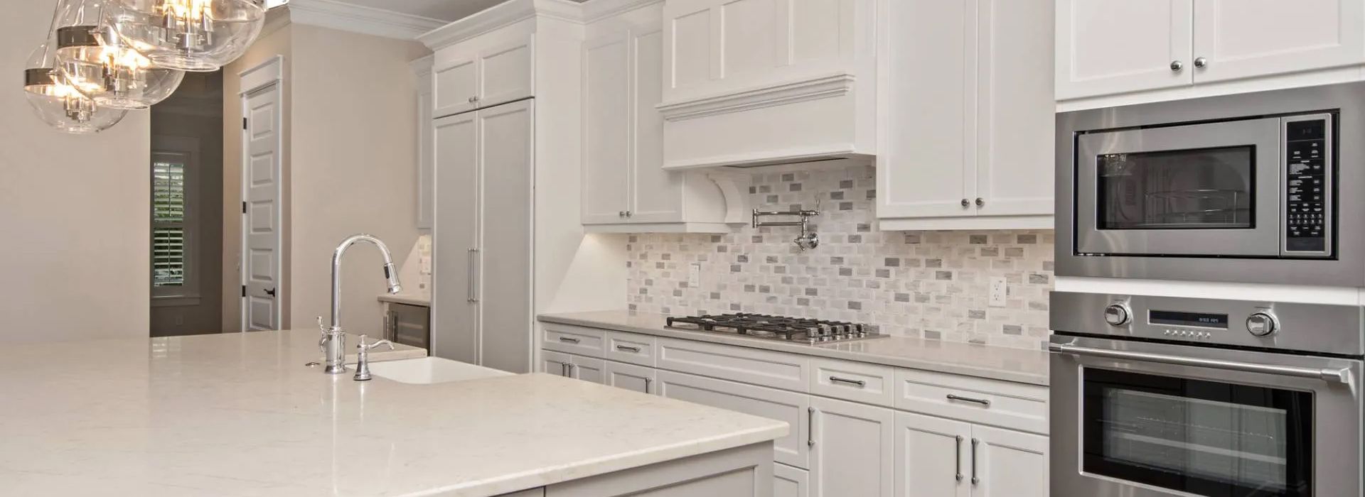 Bright white modern kitchen with marble island, built-in oven, and mosaic tile backsplash