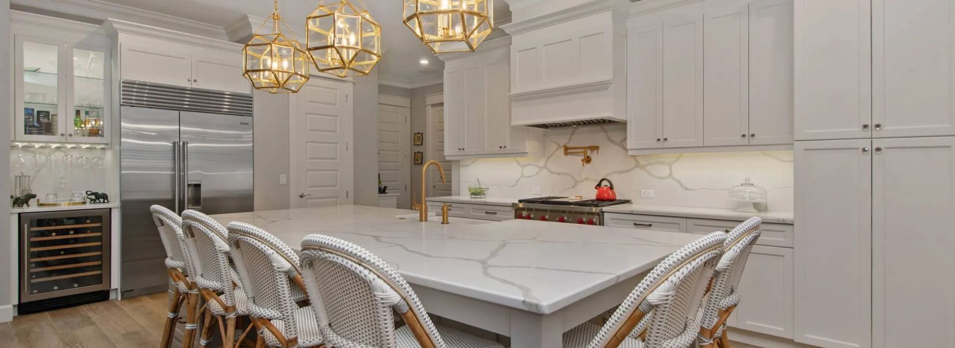 Elegant white kitchen with marble island, gold pendant lights, and wicker barstools